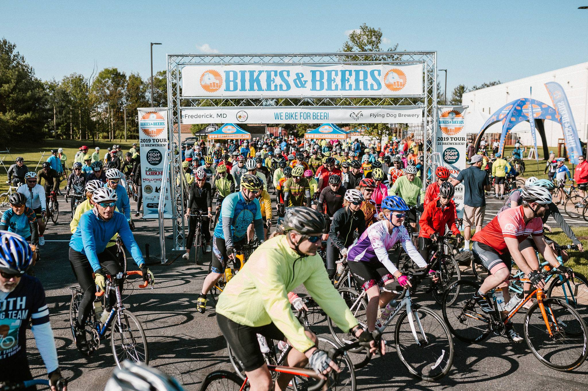 Cyclists gathering at a coastal ride start with event tents and bikes